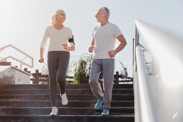 Sporty senior smiling couple in sportswear jogging along urban street having sport workout in the city. Elderly man and woman running outdoors. Jog workout for retired active people concept.