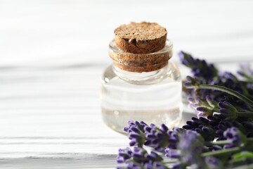 Natural essential oil and lavender flowers on white wooden table, closeup. Space for text