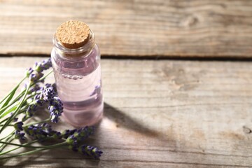 Natural essential oil and lavender flowers on wooden table, closeup. Space for text