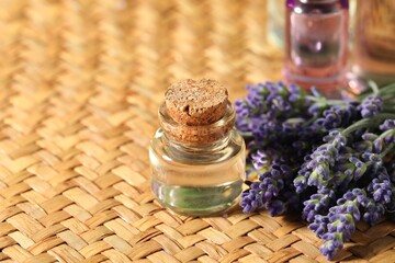Bottles of lavender essential oil and flowers on wicker table, closeup. Space for text