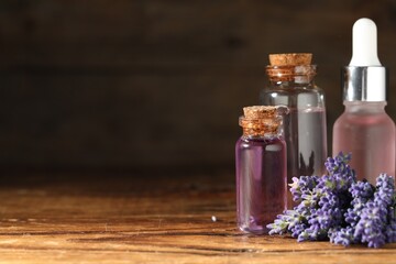 Bottles of lavender essential oil and flowers on wooden table, closeup. Space for text
