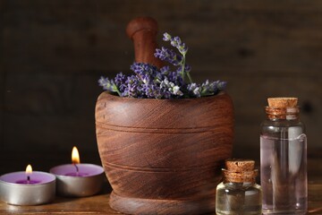 Bottles of lavender essential oil, burning candles and flowers on wooden table, closeup