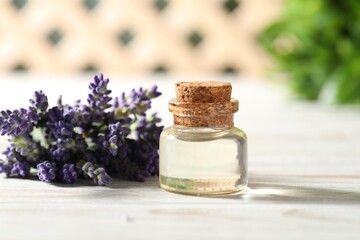 Bottle of essential oil and flowers on white wooden table, closeup