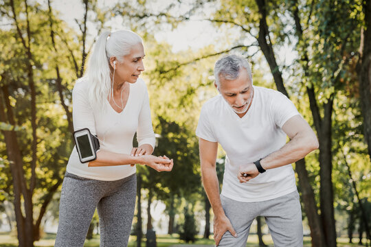 Senior couple, mature woman and man running in park wearing sportswear, training together check the pulse. Morning training workout fitness exercising, sport hobby lifestyle health care concept