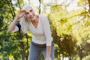 Athletic mature woman resting after jogging. Beautiful senior woman running at the park on a sunny...