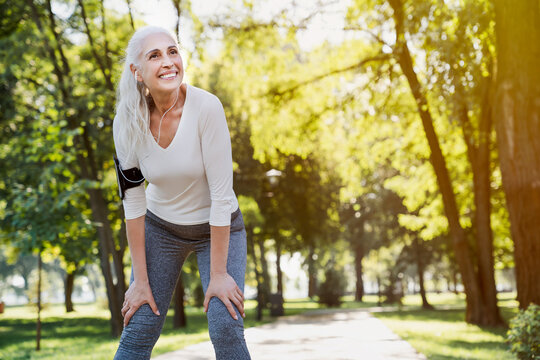 Active hobby on retirement. Rehabilitation health care concept. Grey haired caucasian woman jogging at summer park. Fitness retired female in sport attire taking break after morning run. - Powered by Adobe