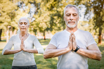 Yoga on retirement. Front view of mature man and woman dressed in sportswear keeping hands in...