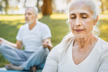 Calm elderly retired family couple people practicing yoga outside happy husband and wife sitting on mats barefoot in lotus position and keeping hands in mudra gesture. Meditation and mental health