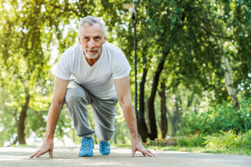 Handsome Caucasian gray haired bearded senior athletic man, runner in sportswear, stands at the...