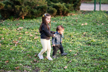Older sister helping younger brother learning to walk in park