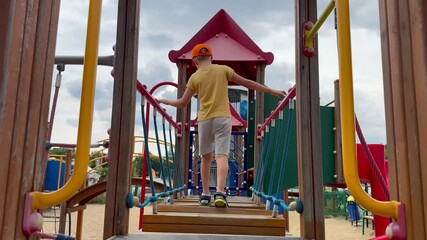 Little boy walks backward on ladder at playground. Young boy carefully walks backward on playground ladder. Coordination, focus, active play, childhood motion, balance and challenge in outdoor space.
