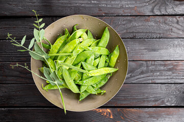 fresh ripe green pea pods on a metal plate and dark wooden background top view