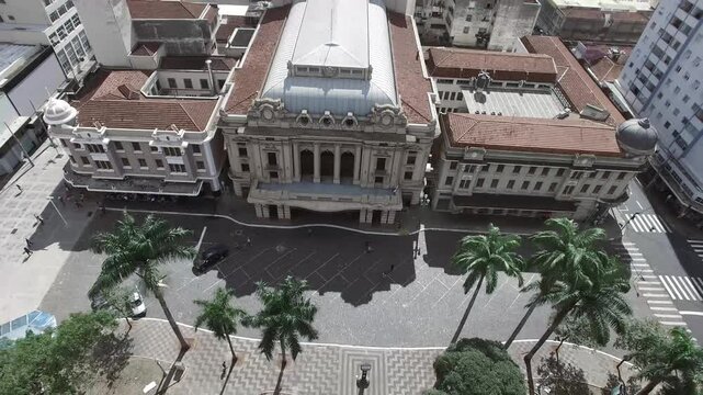 Aerial view of Theatro Pedro II in Ribeir&atilde;o Preto, Brazil. Historic landmark with neoclassical architecture, red-tiled roof, palm trees, and surrounding cityscape on a sunny day.