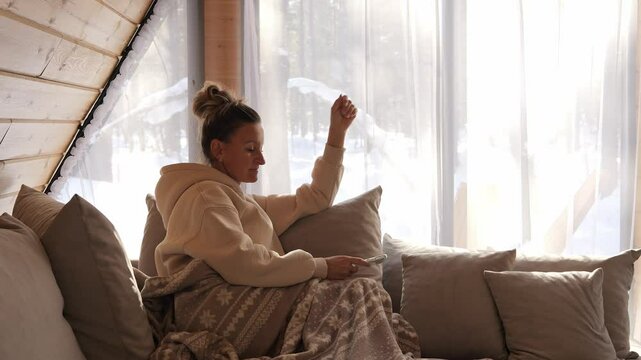 Woman wrapped in soft blanket stares into phone screen in quiet space Digital focus remains present even during mindful pause Blanket brings warmth blanket frames contrast of stillness and technology