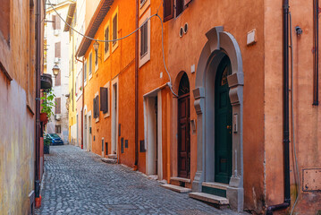 Charming narrow cobblestone street with colorful and terracotta buildings, rustic wooden shutters, arched doorways, and traditional European architecture in Rome, Italy. Travel destination in Europe