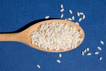 top view of a wooden spoon of raw rice on blue background