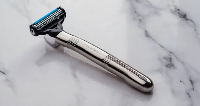 A chrome-plated razor lies on a white marble surface