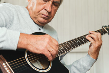 Senior man is playing guitar. Elderly male sitting at sofa and play music. Portrait of a gray...