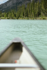 Fototapeta premium Canoe gliding on turquoise lake with forest and mountains ahead with copy space
