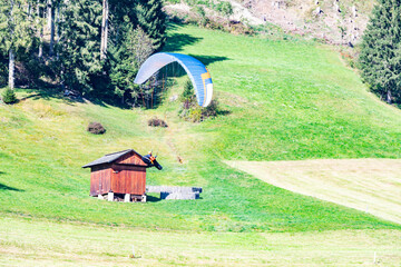 Dynamic shot of paragliding in the Italian Alps. A vibrant paraglider hovers over a green meadow...