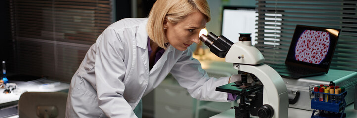 Website header shot of Caucasian middle aged woman examining sample through microscope in...