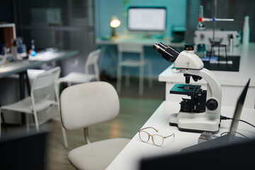 Laboratory microscope standing on workstation with eyeglasses nearby in scientific laboratory,...