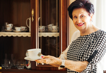 Smiling senior woman showing vintage teacup in living room