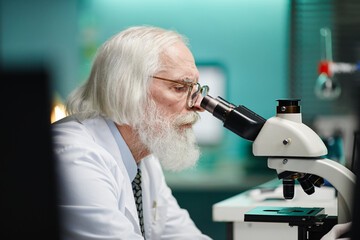 Senior Caucasian man with long hair and beard examining sample using microscope in scientific...