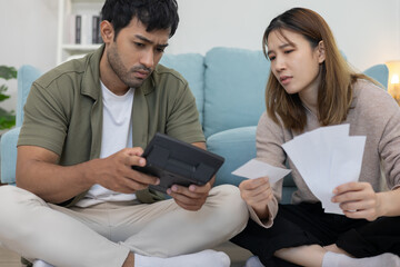 Stressed and headache asian couple with large bills or invoices no money to pay to expenses and...