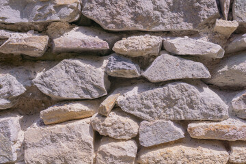 Ancient castle wall made of various sized grey and beige stones, forming a rustic textured background, suitable for historical tourism, architectural preservation, and building material suppliers