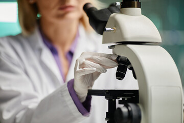 Caucasian middle aged woman adjusting microscope in scientific laboratory, wearing lab coat and...
