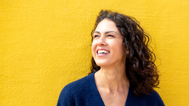 Close-up of a smiling woman looking upward, standing against a vivid yellow wall