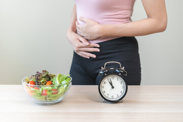 Intermittent fasting, diet healthy asian young woman dietary, having stomach ache, temptation hungry of brunch food in morning on table at home, waiting time to eat salad but not yet time first meal.