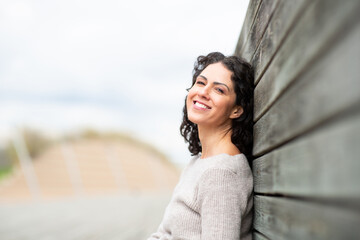 Woman leaning against a weathered wooden wall, smiling warmly at the camera