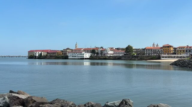 A wide, panoramic view of the historic Casco Viejo (Old Quarter) of Panama City, with its charming colonial buildings and churches, bordering the calm blue waters of the bay.