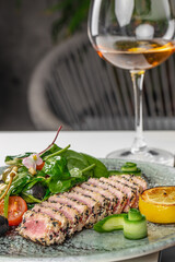 A gourmet dish of sesame-crusted seared tuna served with a fresh spinach and olive salad, cherry...
