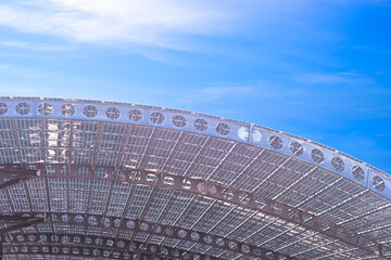 Many solar panels on top of curve roof beams structure made from metal cellular beam against blue sky background, low angle view with copy space