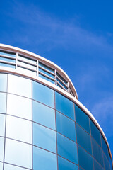 Modern curve geometric office building with blue sky reflection on glass wall surface, view from below and vertical frame