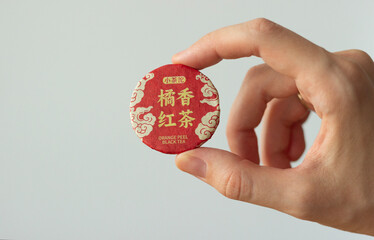 hand holding a disc of compressed chinese orange peel black tea, isolated on neutral background