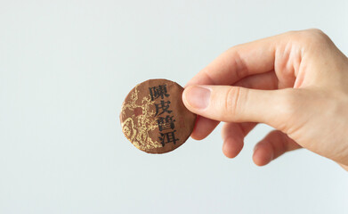 hand holding a round compressed disc of traditional chinese tea for tea ceremony, isolated on white