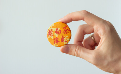 hand holding an orange package of chinese compressed tea, isolated on neutral color