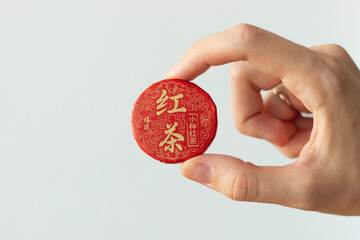 hand holding a package of traditional black chinese tea for tea ceremony, tea disc, tea brick, black tea, isolated on white