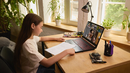 Girl attentively participates in an online class, studying electronics with a circuit board beside...
