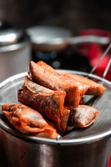 Crispy golden spring rolls draining oil on a metal strainer in a home kitchen setting. Perfect for culinary, Asian food, or cooking themes.