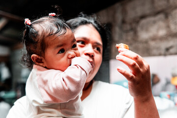 A loving Indonesian mother holding her baby while offering a homemade snack. Perfect for family...