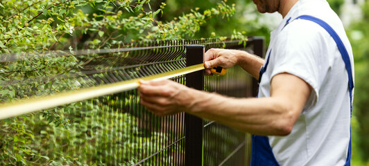 fencing services. worker taking measurements with measuring tape for new fence. banner with copy...