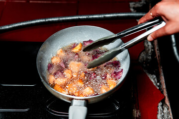 Chunks of purple and yellow sweet potatoes being deep-fried in hot oil on a stovetop. Ideal for food blogs, recipes, culinary tutorials, and Asian home cooking content.