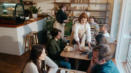 A female employee carries food and napkins to a table where two female customers are sitting and talking