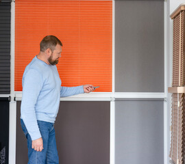 In a showroom filled with motorized blinds and shades, a man uses a remote to demonstrate window blinds. Window treatments store presents modern automation features.