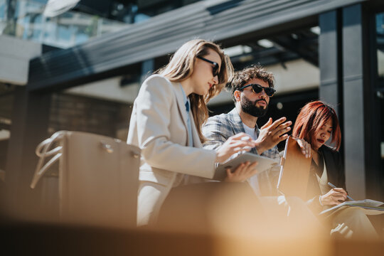 People engaging in a productive business discussion in an urban outdoor setting on a sunny day. They hold digital devices while talking and recording notes, reflecting collaboration and innovation.